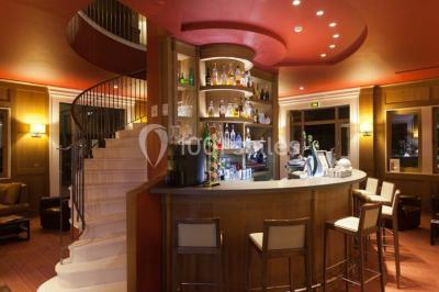 Paysage automnal avec un lac reflétant des arbres aux feuilles rouges et orangées sous un ciel nuageux.