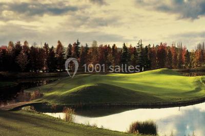 Paysage automnal avec un lac reflétant des arbres aux feuilles rouges et orangées sous un ciel nuageux.