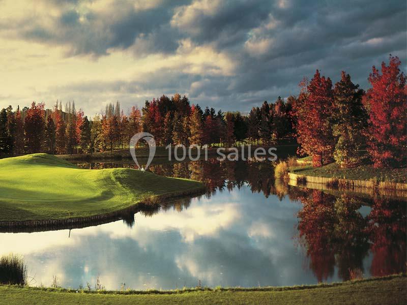 Paysage automnal avec un lac reflétant des arbres aux feuilles rouges et orangées sous un ciel nuageux.