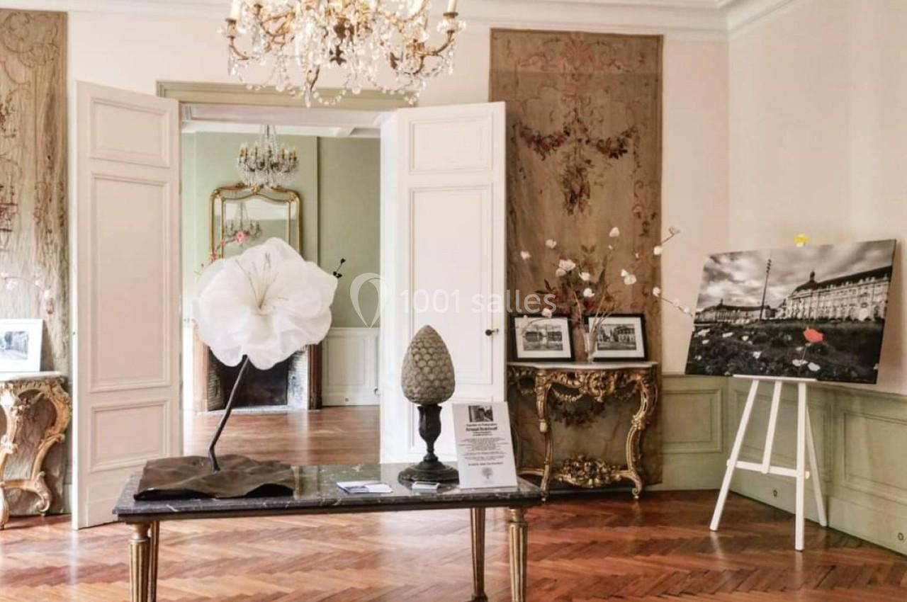 Salle élégante avec parquet en bois, table ornée, lustre, et décorations artistiques sur les murs et meubles.