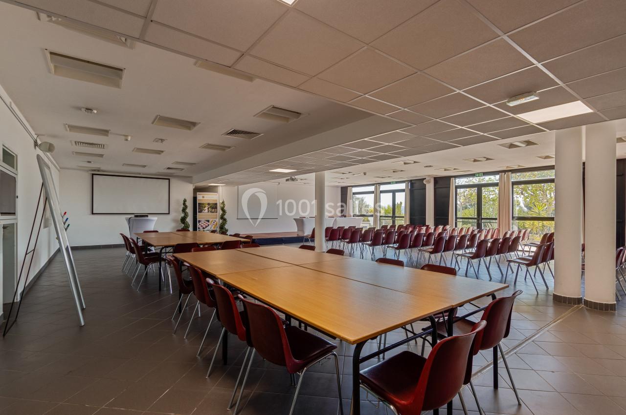 Salle de conférence lumineuse avec chaises alignées, tables en bois et écrans de projection.