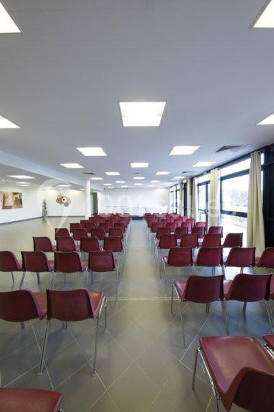 Salle de conférence lumineuse avec des rangées de chaises rouges alignées face à un tableau blanc.
