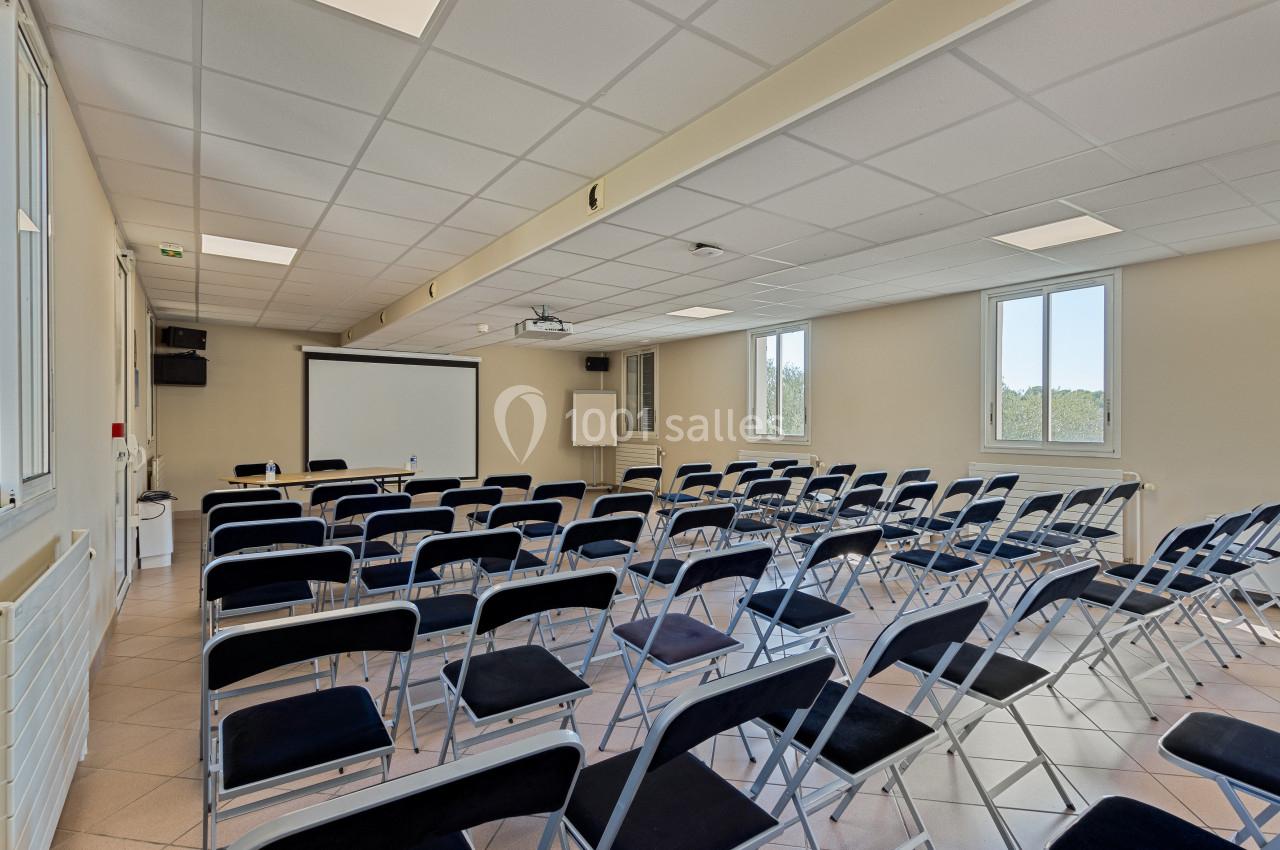 Salle de conférence lumineuse avec rangées de chaises pliantes noires, écran de projection et fenêtres donnant sur l…