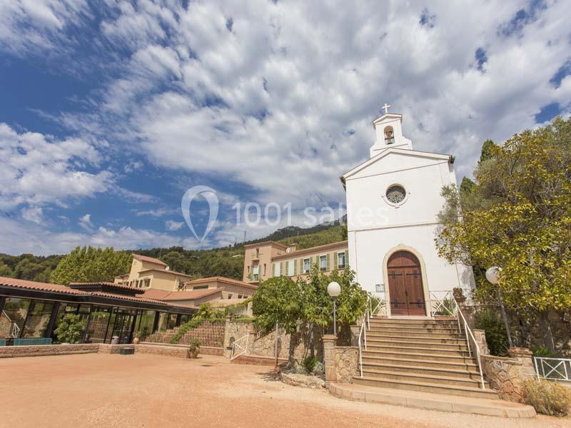 Façade d'une petite église blanche avec un escalier, entourée de bâtiments et de végétation sous un ciel partiellement…