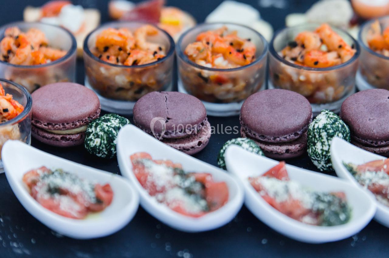 Assortiment de verrines, macarons salés, bouchées de fromage et cuillères apéritives sur une table noire.