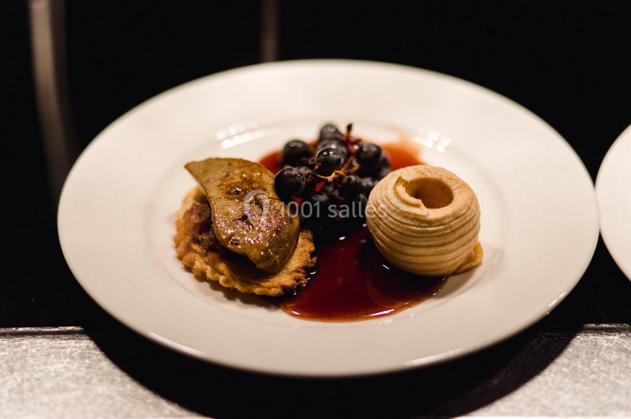 Assiette gastronomique avec foie gras, raisins, sauce et pomme sculptée, présentée sur un fond sombre.
