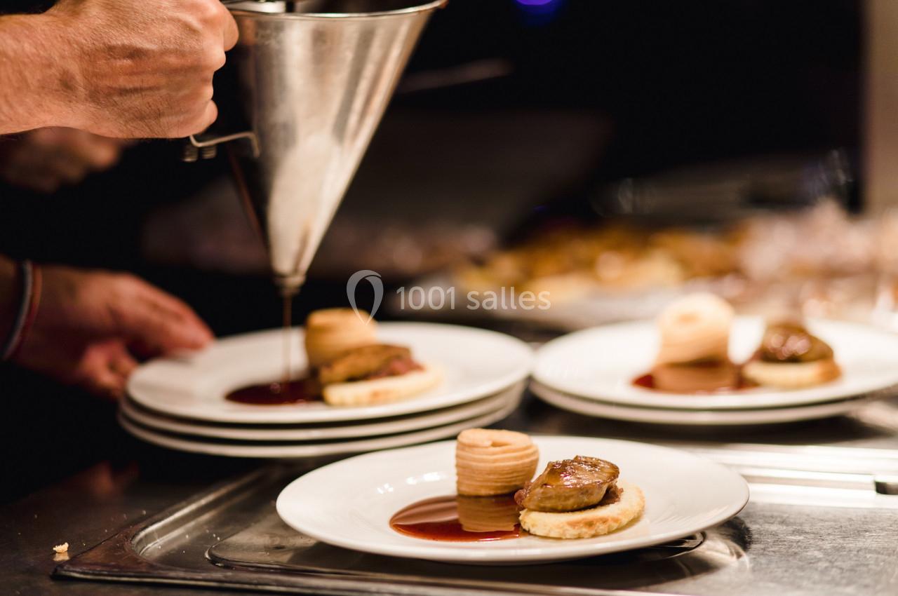 Un chef dresse des assiettes avec du foie gras, une sauce et une garniture élégante dans une cuisine professionnelle.