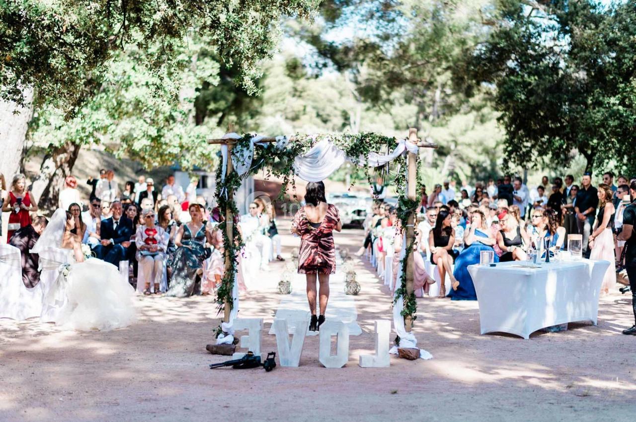 Une cérémonie de mariage en extérieur avec des invités assis, un autel décoré et une personne parlant devant l'assemblée.