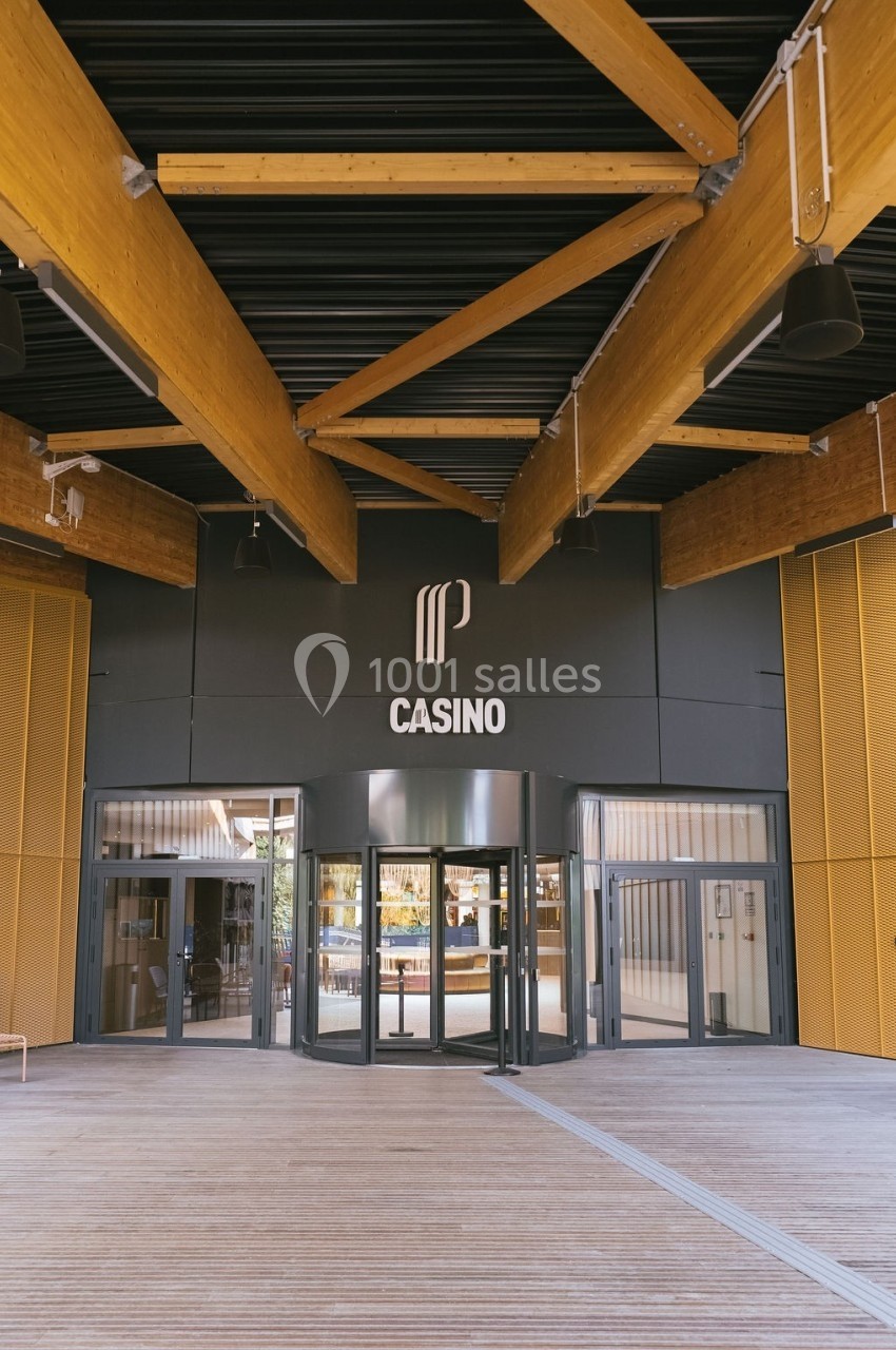 Entrée principale d'un casino moderne avec des structures en bois et un logo visible au-dessus des portes vitrées.