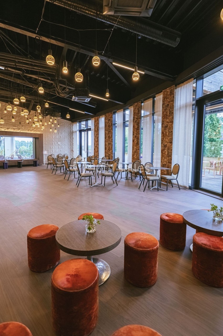 Salle spacieuse avec tables, chaises et tabourets rouges, éclairée par des suspensions et des baies vitrées donnant sur l…