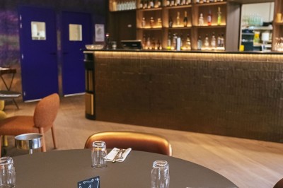 Salle de casino avec table de jeu vide, chaises alignées, machines à sous illuminées et éclairage suspendu moderne.