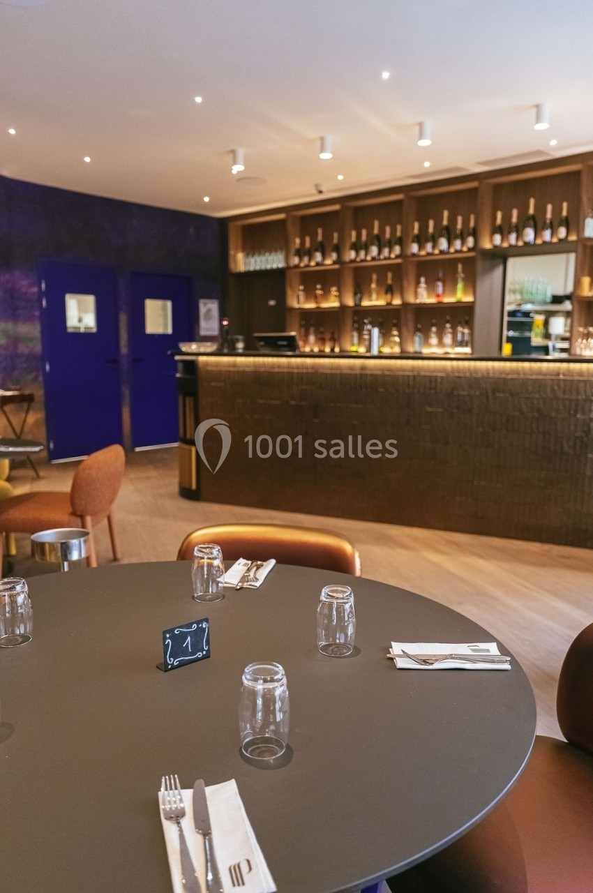 Table dressée avec couverts et verres dans un restaurant moderne, avec un bar en arrière-plan.