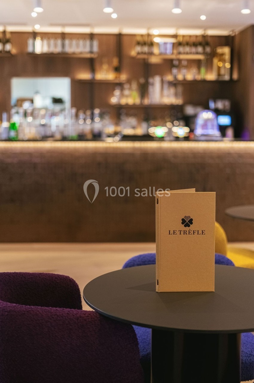 Menu posé sur une table ronde dans un bar élégant avec un comptoir éclairé en arrière-plan.