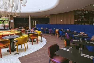 Salle de casino avec table de jeu vide, chaises alignées, machines à sous illuminées et éclairage suspendu moderne.