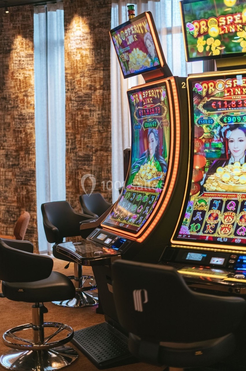 Machines à sous colorées dans un casino, avec des écrans lumineux affichant des jeux et des sièges noirs devant.