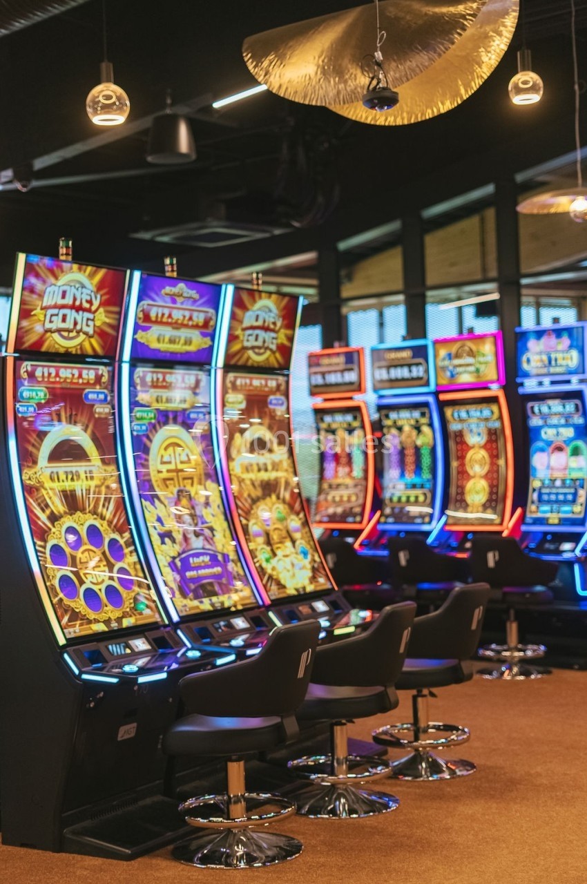 Rangée de machines à sous colorées alignées dans un casino, avec des sièges noirs devant chaque machine.