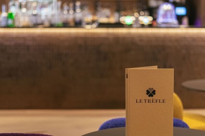 Menu posé sur une table ronde dans un bar élégant avec un comptoir éclairé en arrière-plan.