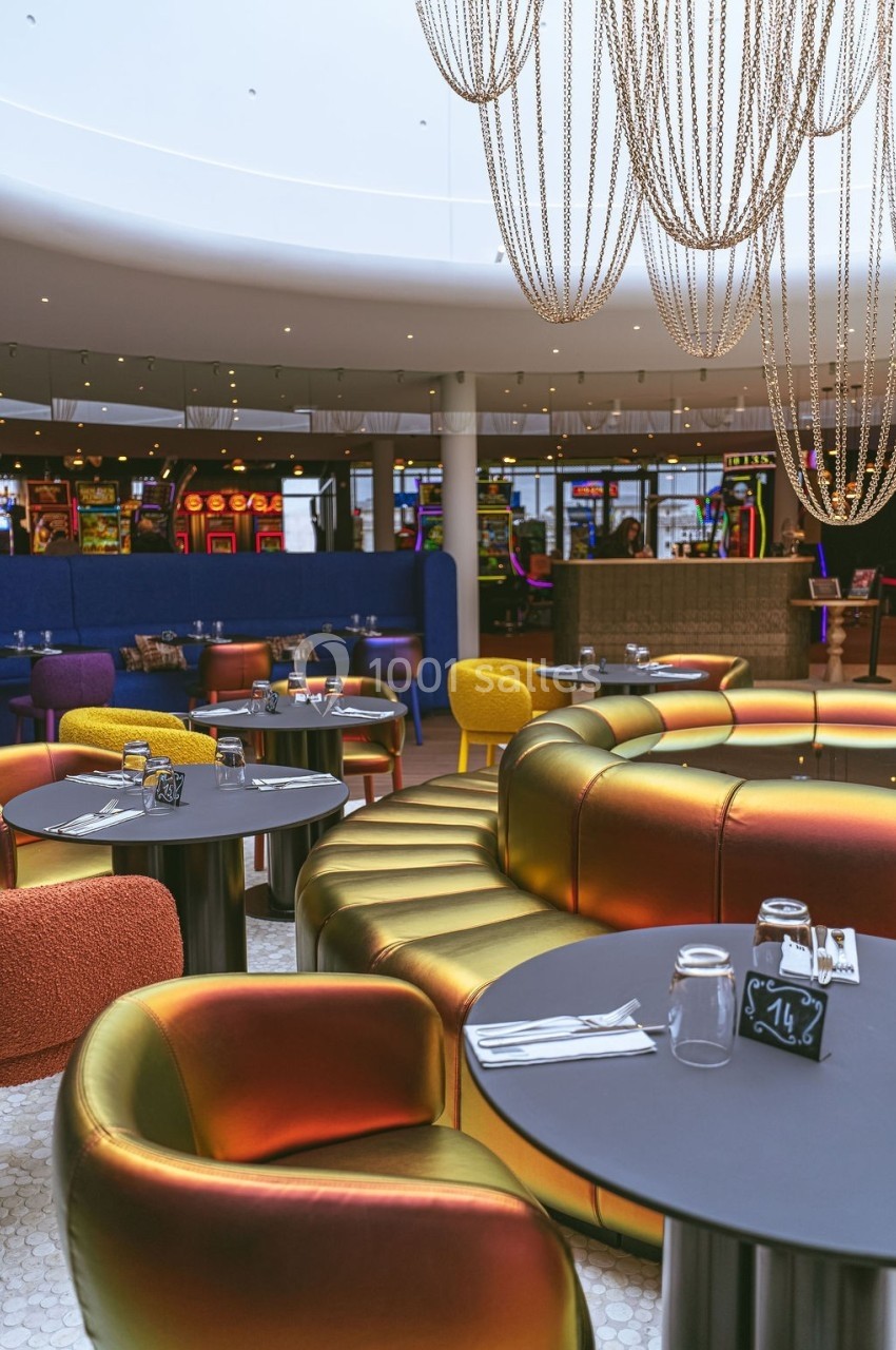 Salle de restaurant moderne avec tables dressées, fauteuils colorés et vue sur des machines à sous en arrière-plan.