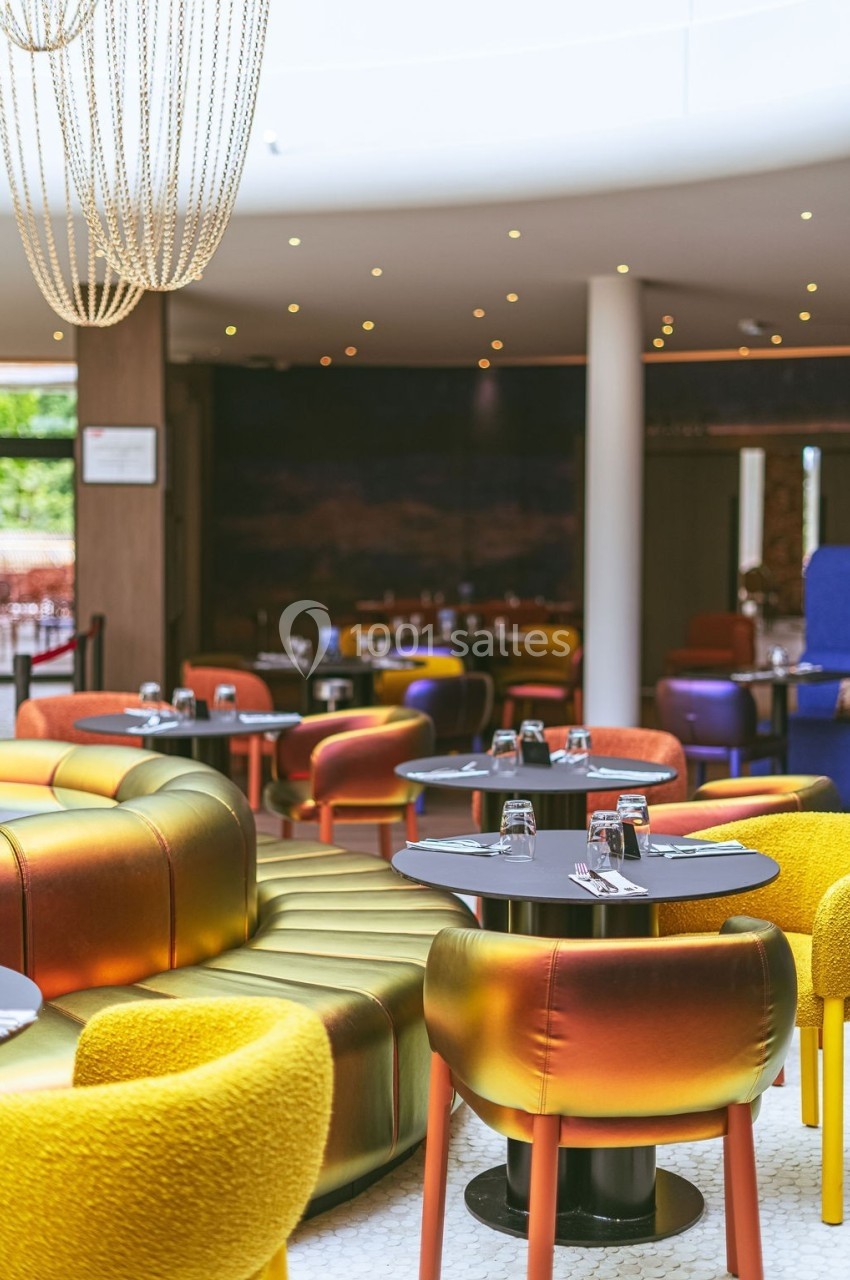 Salle de restaurant moderne avec fauteuils colorés, tables rondes dressées et éclairage tamisé.
