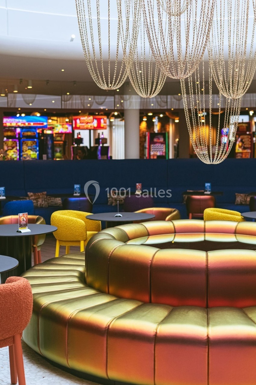 Banquettes circulaires colorées sous des lustres en chaînes, avec des jeux d'arcade en arrière-plan.