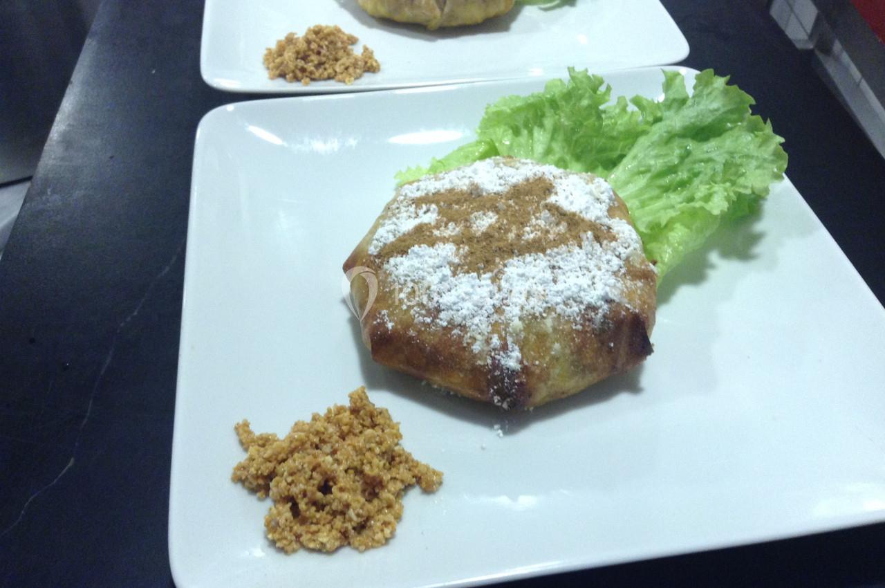 Plat de pastilla saupoudrée de sucre glace, servie avec une feuille de laitue et une garniture croustillante.
