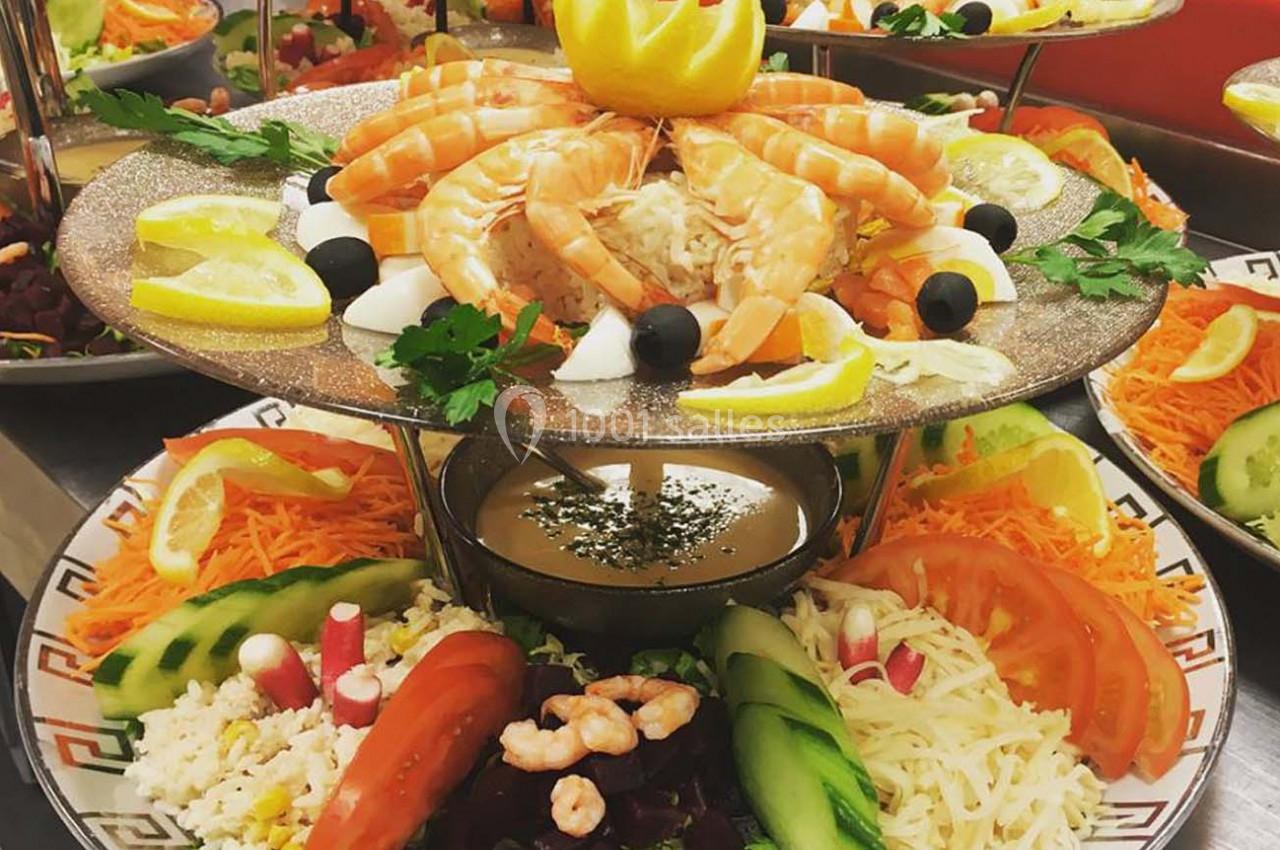 Plateau de fruits de mer avec crevettes, saumon, légumes frais et sauce, présenté sur un support décoratif.