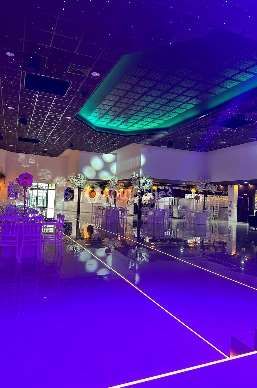 Salle de réception moderne avec éclairage violet, plafond étoilé et tables décorées de fleurs blanches.