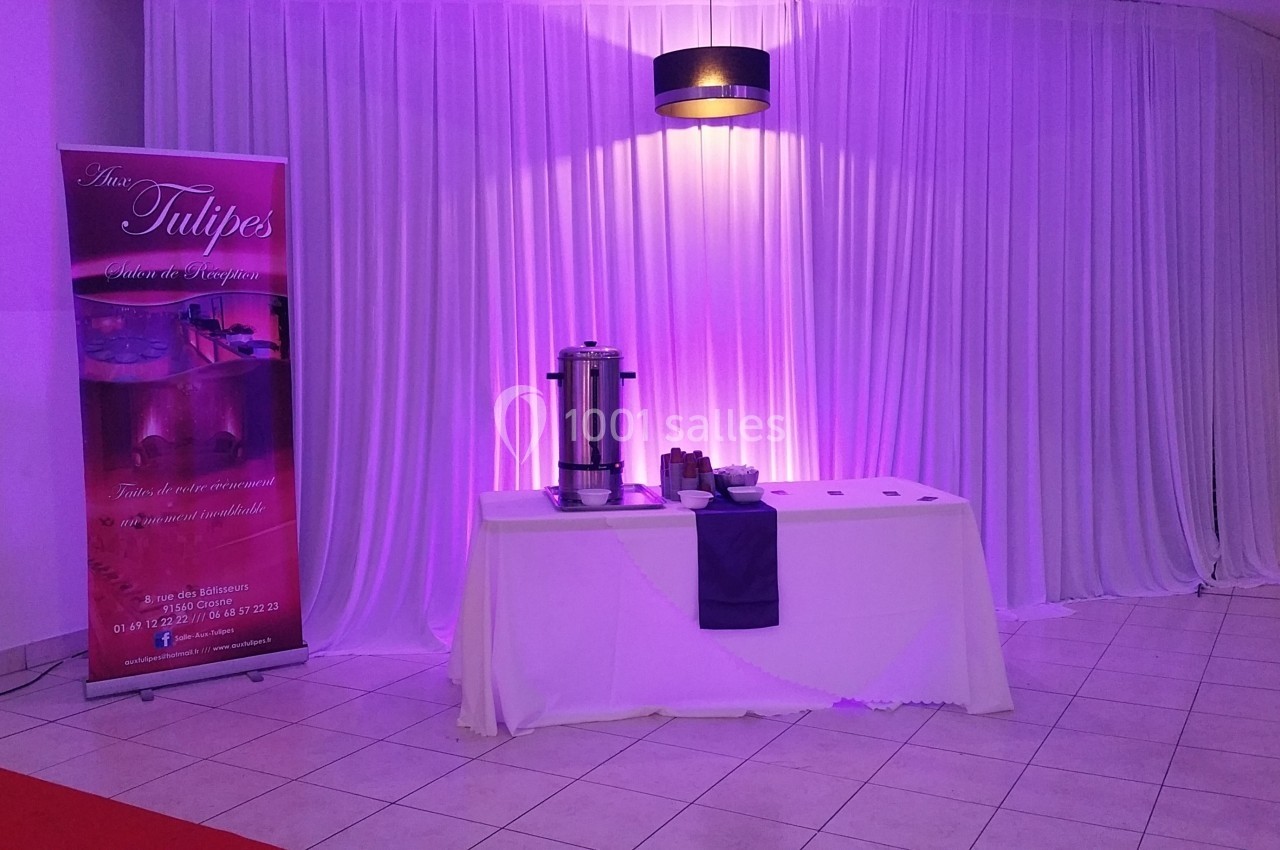 Table de service avec une cafetière et des accessoires, devant un rideau blanc éclairé de lumières violettes.