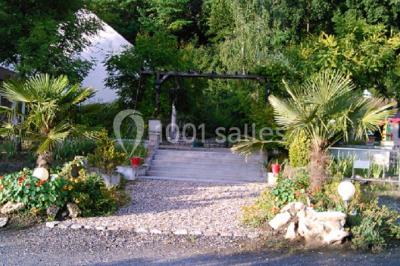 Portail en fer forgé rouge avec piliers blancs, donnant sur une allée menant à une maison entourée d'arbres.