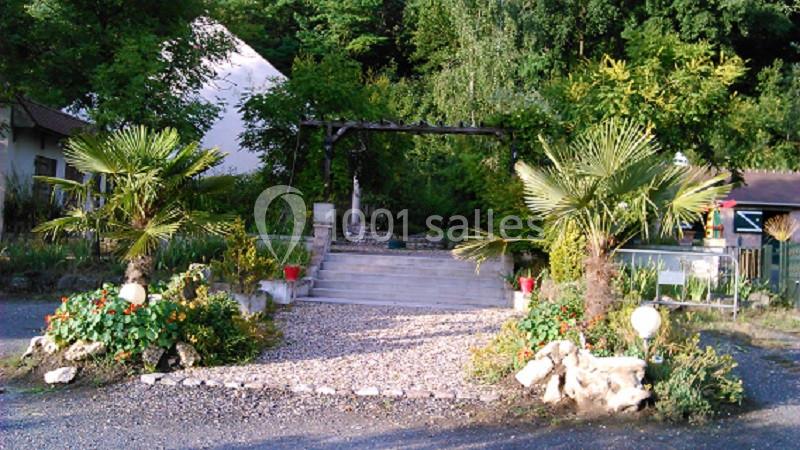Allée en gravier bordée de palmiers et de plantes, menant à un escalier en pierre entouré de verdure.