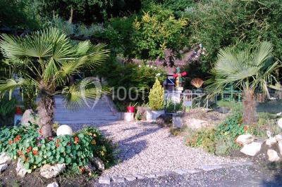 Portail en fer forgé rouge avec piliers blancs, donnant sur une allée menant à une maison entourée d'arbres.