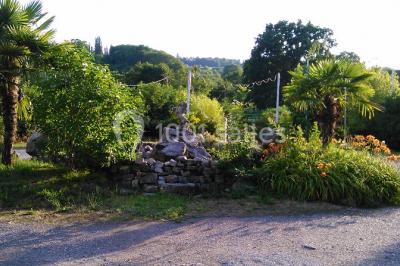 Portail en fer forgé rouge avec piliers blancs, donnant sur une allée menant à une maison entourée d'arbres.