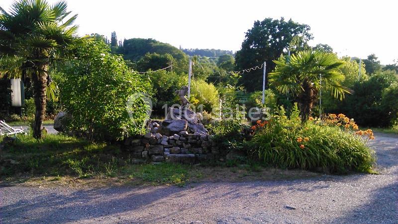 Jardin avec palmiers, fleurs orange, buissons verdoyants et un petit monticule de pierres au centre.