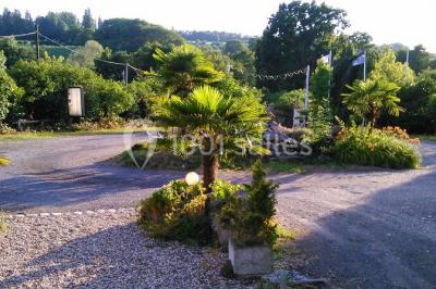Portail en fer forgé rouge avec piliers blancs, donnant sur une allée menant à une maison entourée d'arbres.