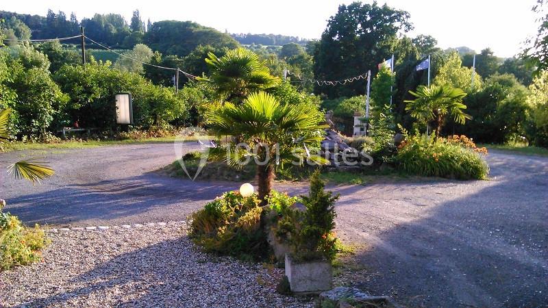Allée gravillonnée bordée de végétation luxuriante, avec des palmiers et un paysage verdoyant en arrière-plan.