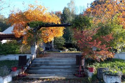Portail en fer forgé rouge avec piliers blancs, donnant sur une allée menant à une maison entourée d'arbres.