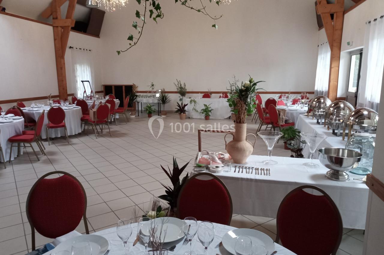 Salle de réception lumineuse avec tables dressées, chaises rouges, buffets en inox et décorations végétales.