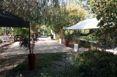 Portail en fer forgé rouge avec piliers blancs, donnant sur une allée menant à une maison entourée d'arbres.