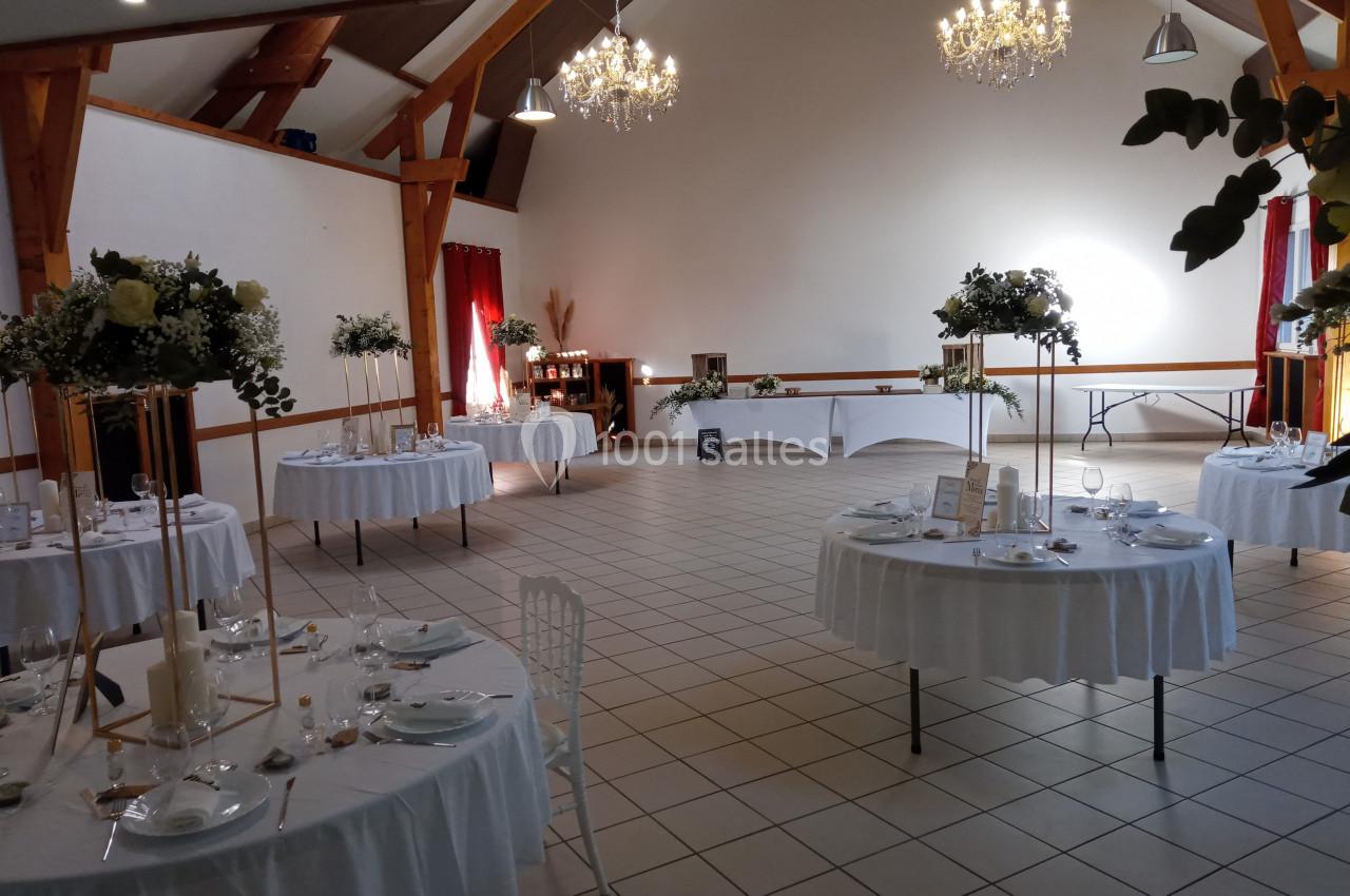 Salle de réception décorée avec des tables rondes dressées, des chandeliers et des compositions florales.