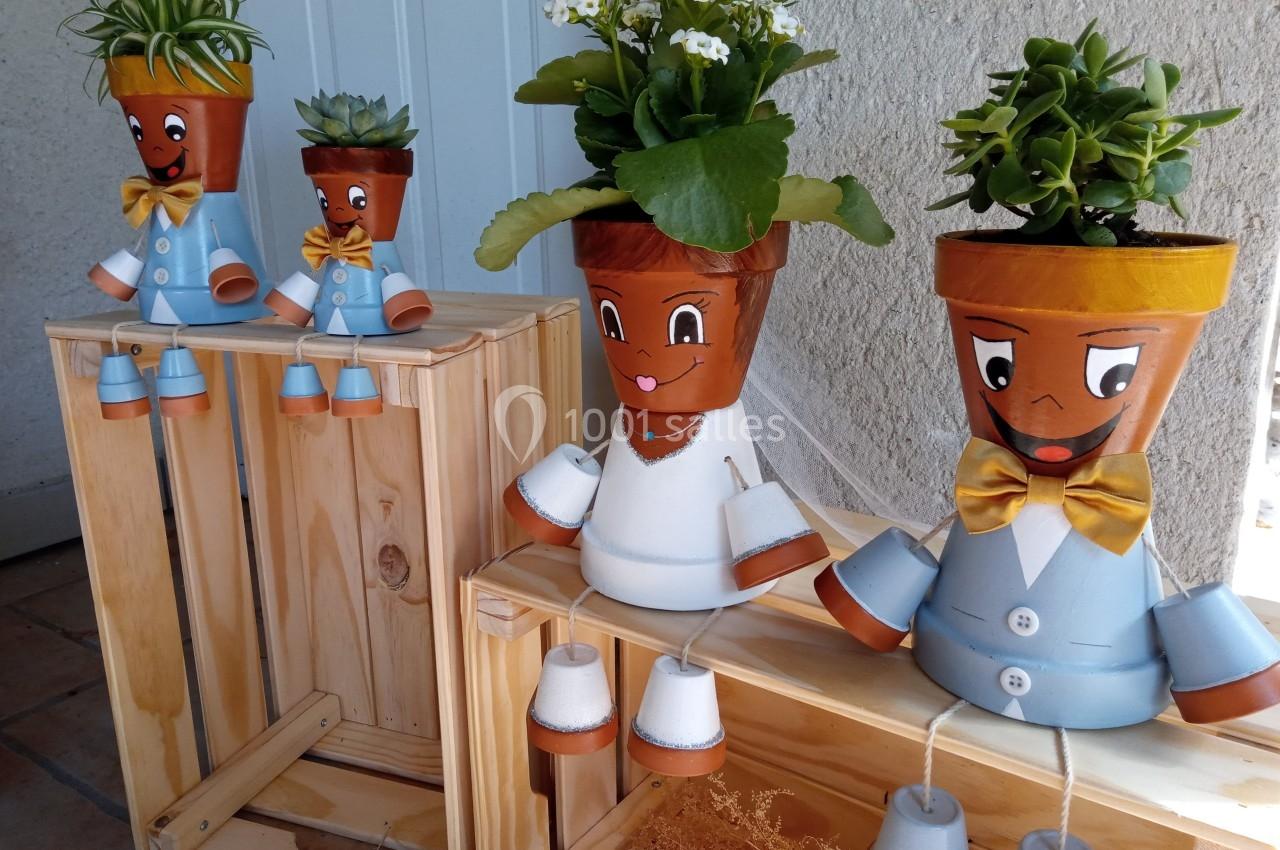 Pots en terre cuite peints en forme de personnages, décorés avec des plantes, posés sur des caisses en bois.