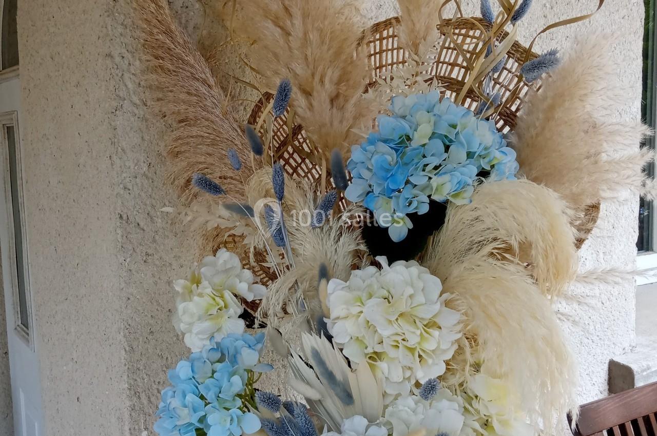 Composition florale avec des fleurs blanches et bleues, pampas et éléments décoratifs dans un vase en terre cuite.