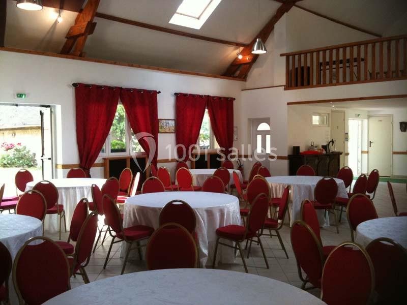 Salle lumineuse avec tables rondes dressées de nappes blanches et chaises rouges, décorée de rideaux rouges et poutres…