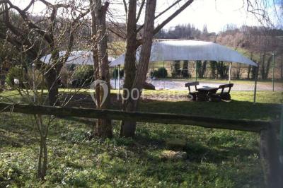 Portail en fer forgé rouge avec piliers blancs, donnant sur une allée menant à une maison entourée d'arbres.