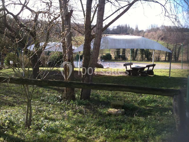 Vue d'un espace extérieur avec des tables en bois, des arbres et une structure couverte près d'un plan d'eau.