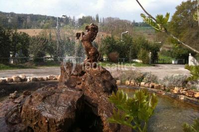 Portail en fer forgé rouge avec piliers blancs, donnant sur une allée menant à une maison entourée d'arbres.