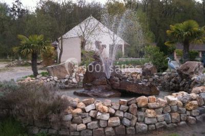 Portail en fer forgé rouge avec piliers blancs, donnant sur une allée menant à une maison entourée d'arbres.