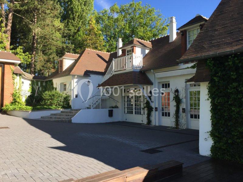 Façade d'une maison blanche avec toits en tuiles, escaliers extérieurs et végétation environnante.