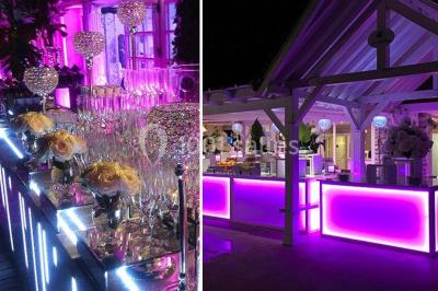 Pont éclairé et kiosque en bois près d'une fontaine illuminée, entourés d'arbres dans un parc nocturne.