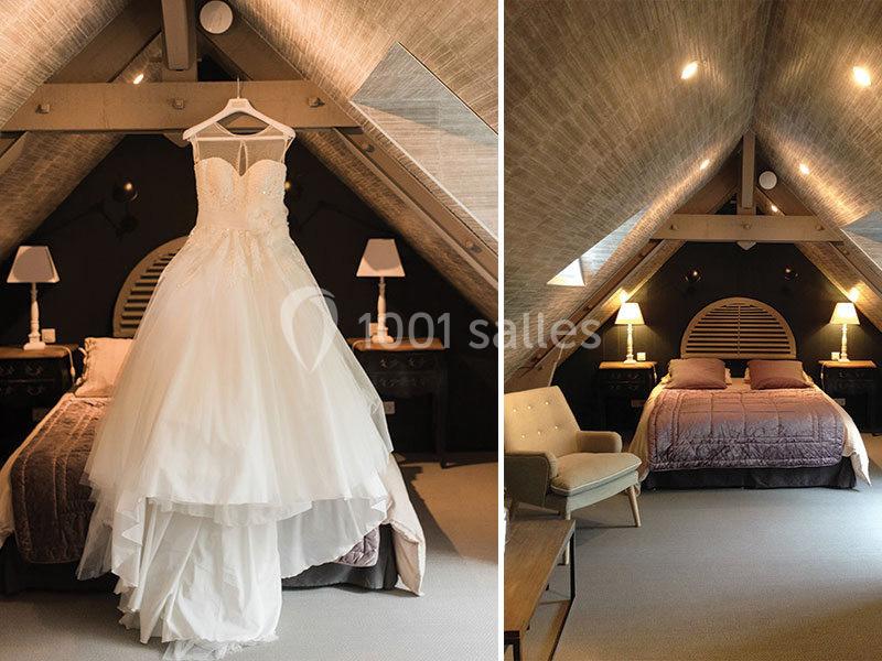 Robe de mariée suspendue dans une chambre mansardée avec un lit double et des lampes de chevet allumées.