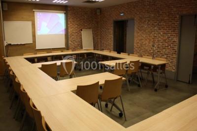 Salle de conférence vide avec des rangées de chaises en bois, un écran de projection et des tableaux accrochés au mur.